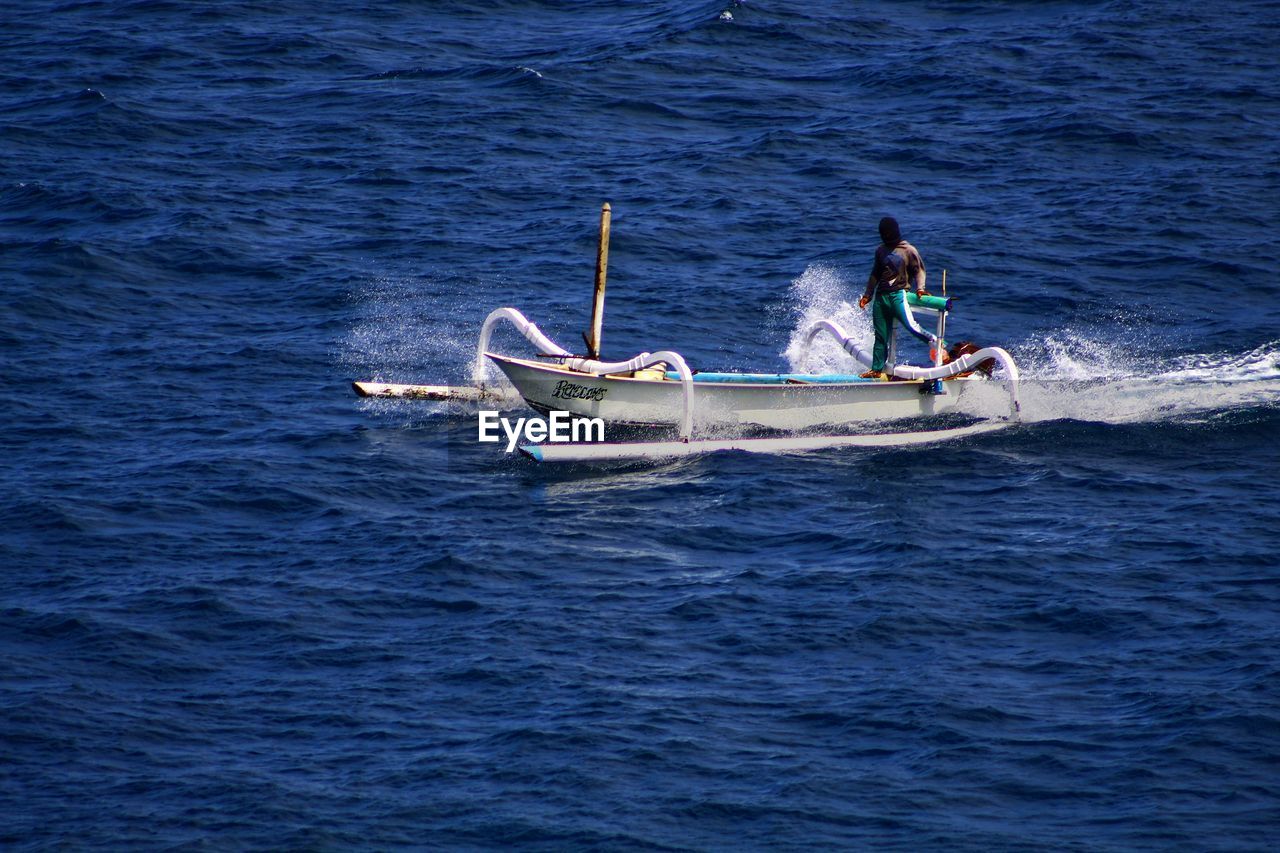 MAN SAILING ON SEA AGAINST BOAT