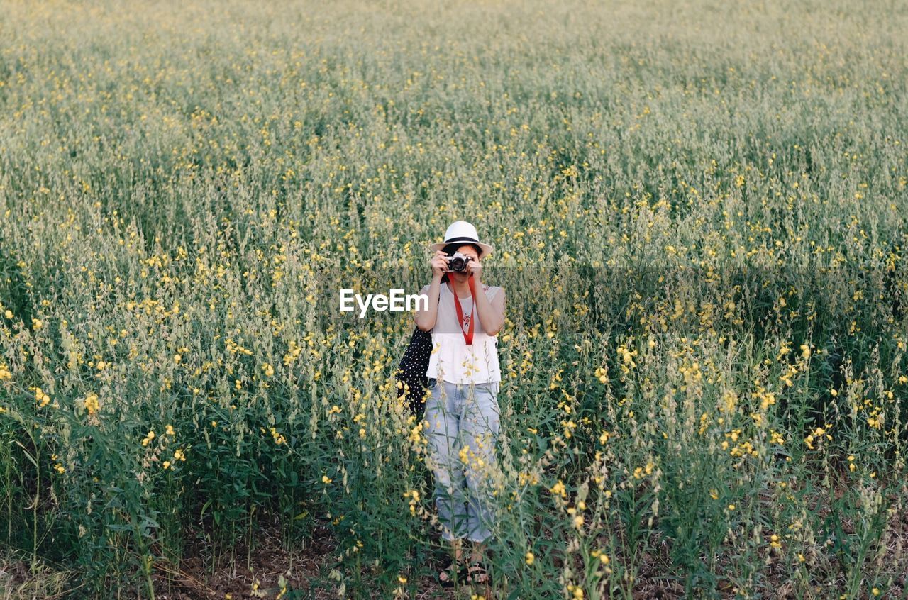 Full length of woman photographing while standing on field