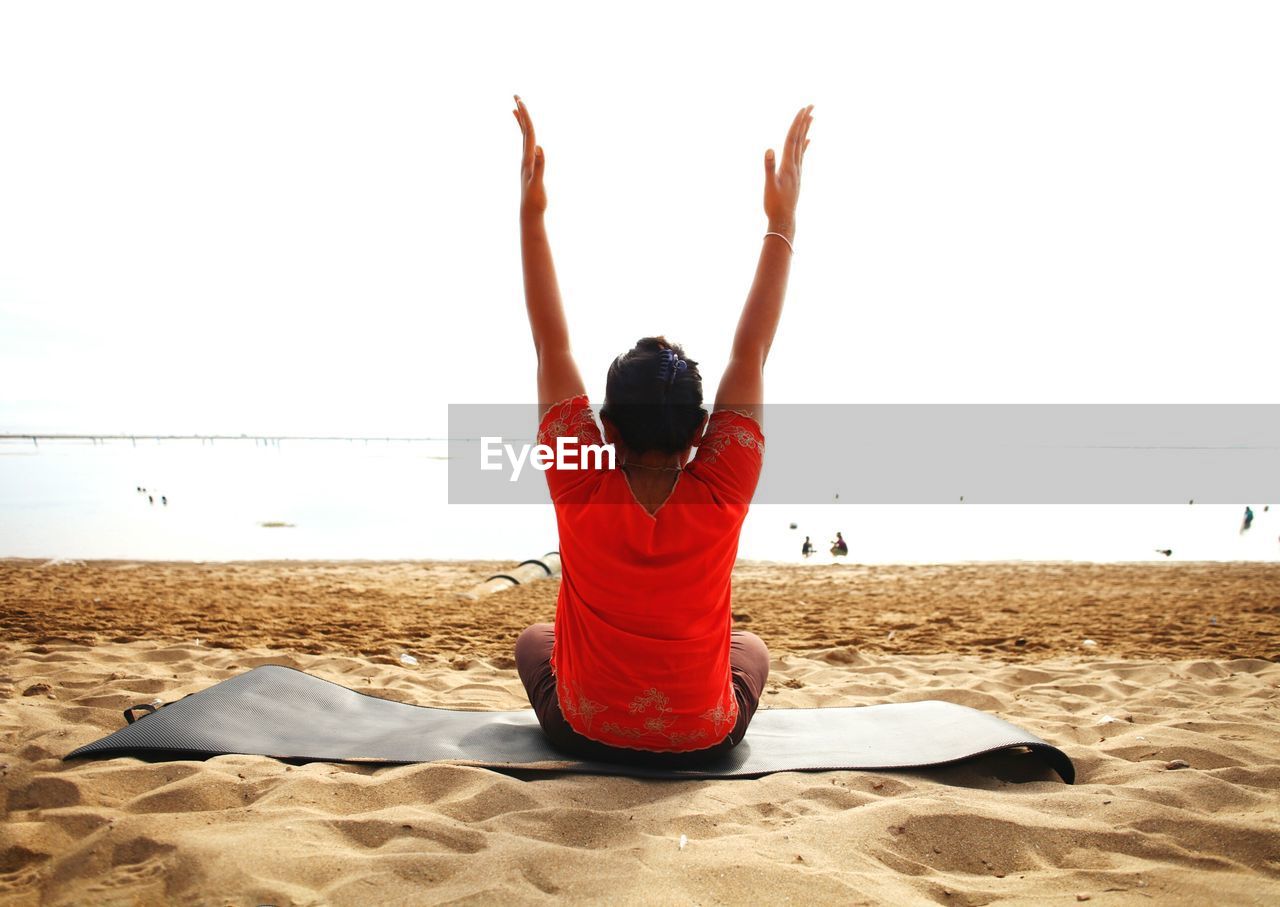 Rear view of woman practicing yoga at beach against clear sky