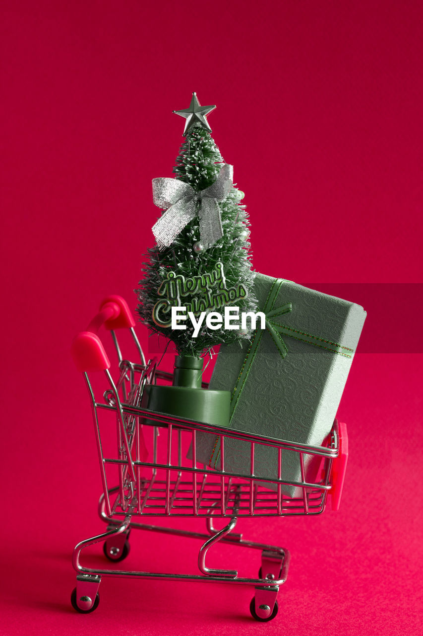 Small christmas tree and gift in shopping cart against pink background