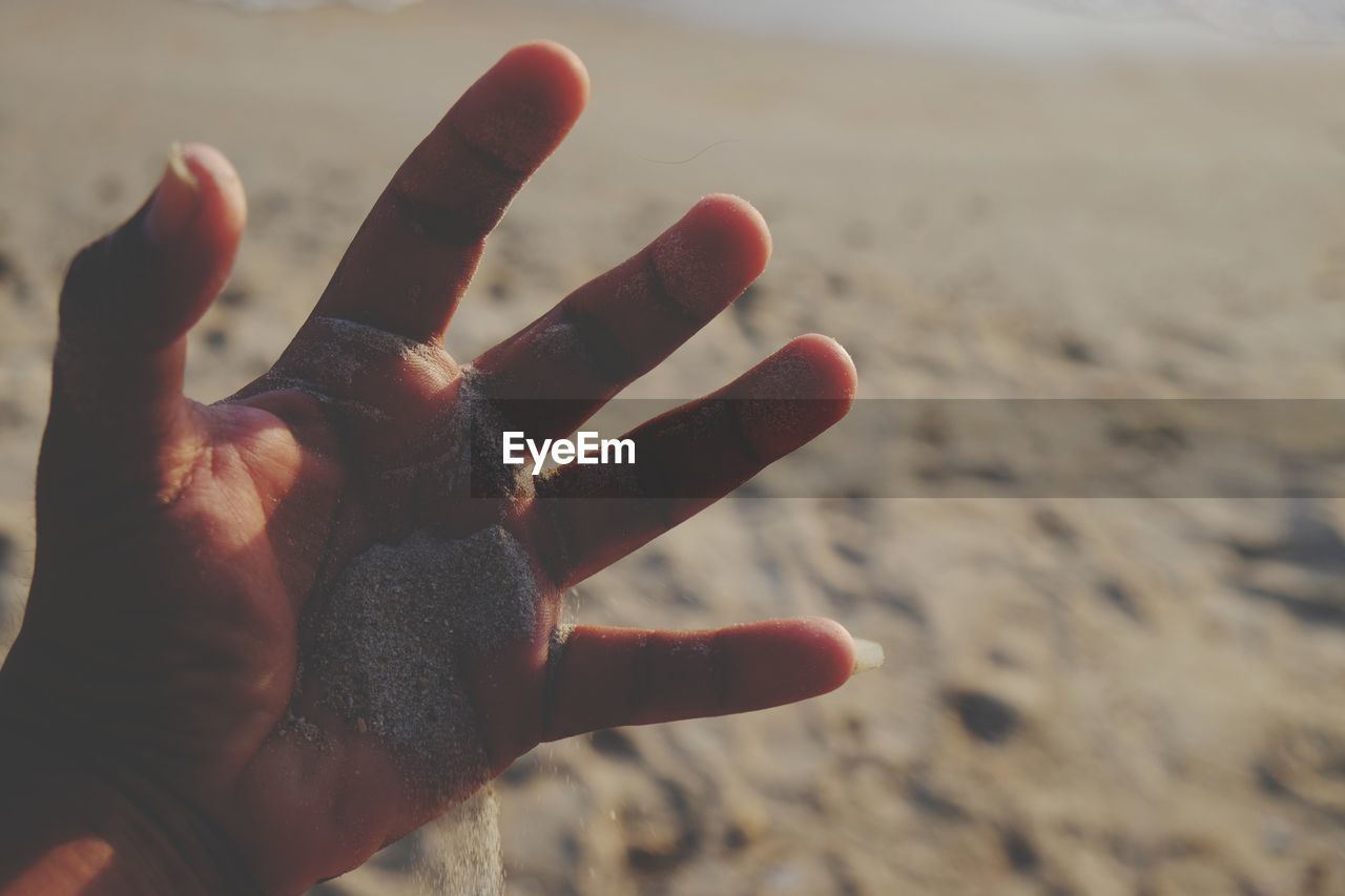 CLOSE-UP OF HUMAN HAND ON SAND