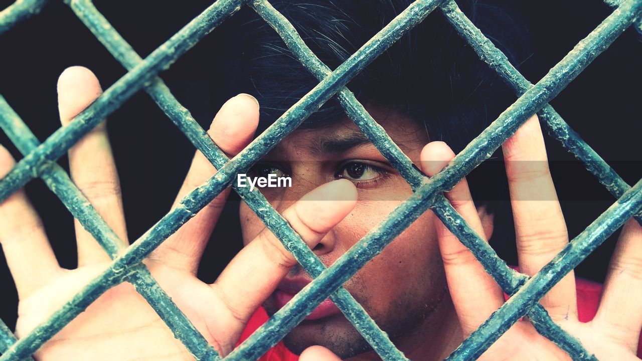 CLOSE-UP PORTRAIT OF MAN BEHIND FENCE