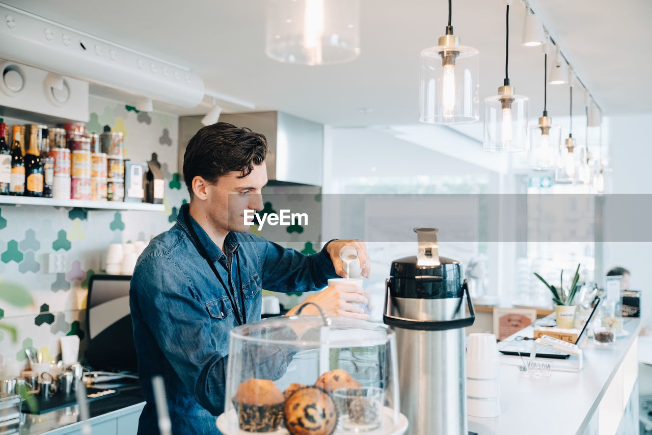 Young owner making coffee at checkout counter in office cafe