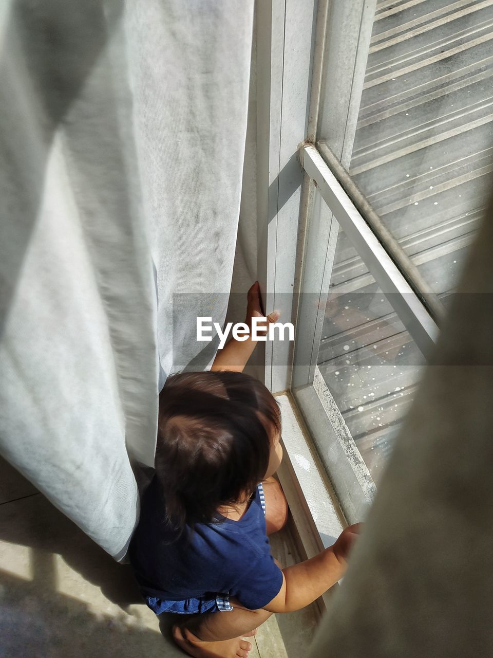 High angle view of boy crouching by window at home
