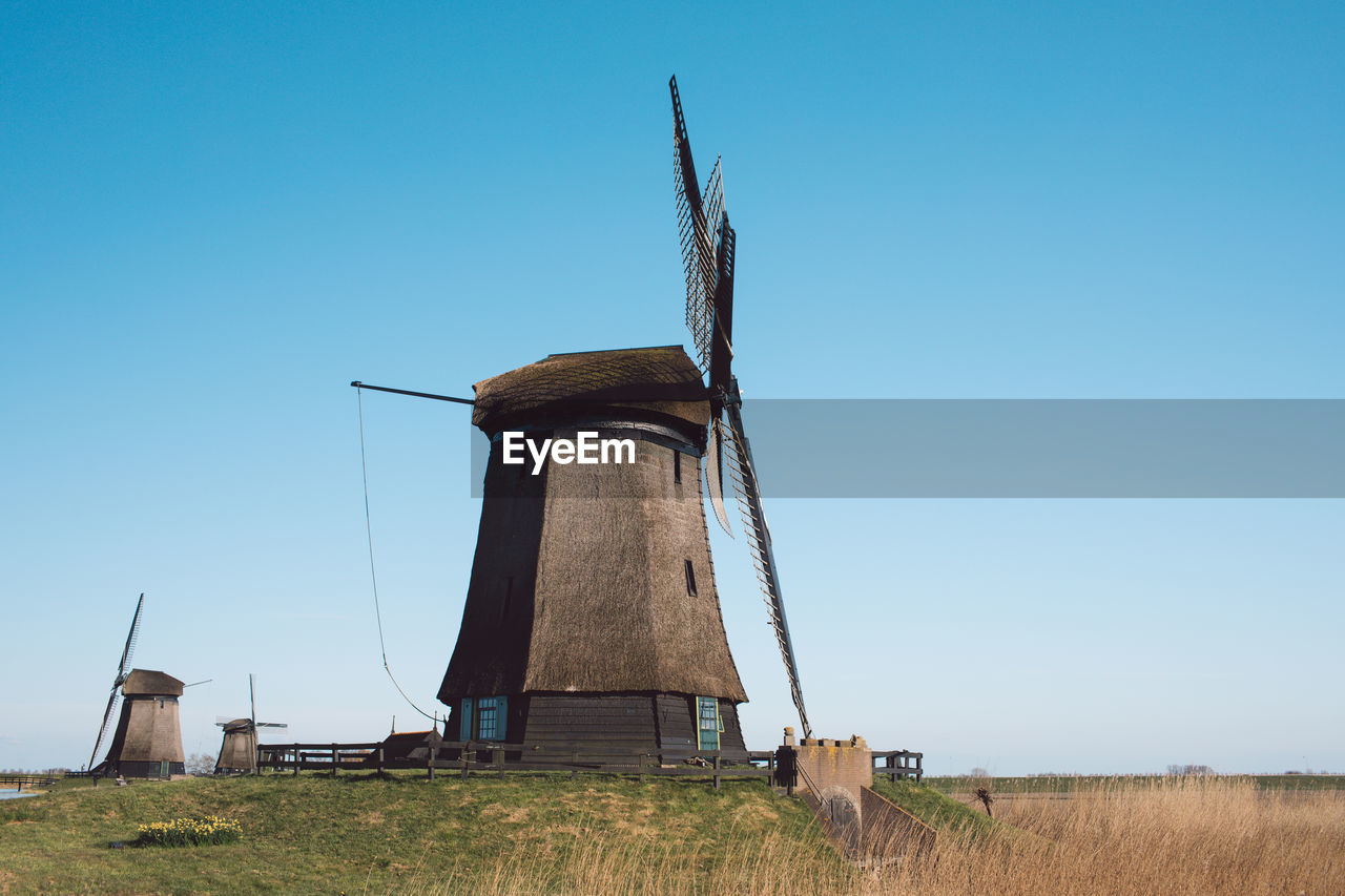 Traditional windmill on field against clear blue sky