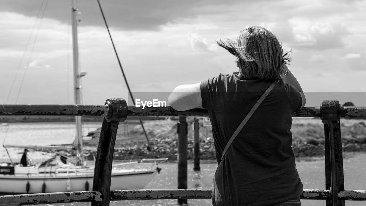 Rear view of woman standing by railing against cloudy sky