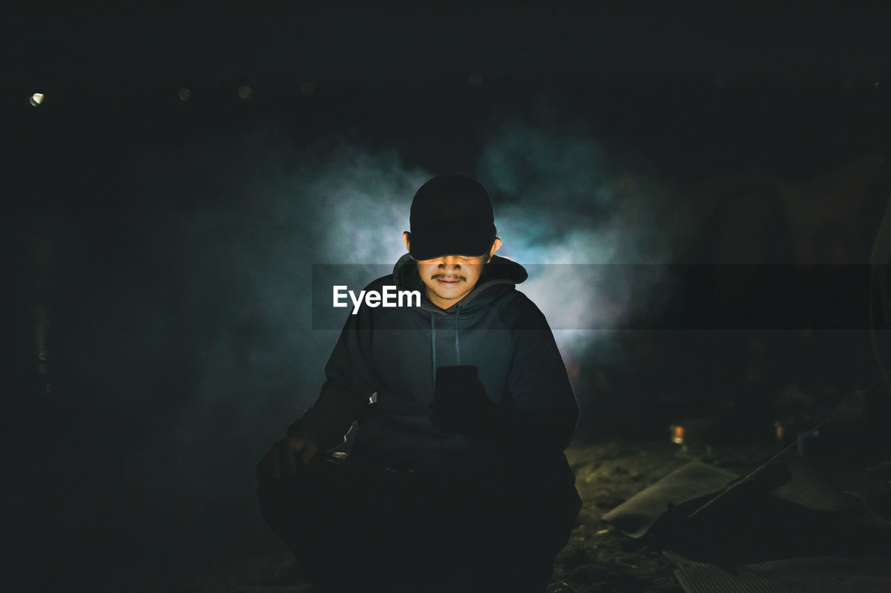 Man using mobile phone while sitting outdoors at night