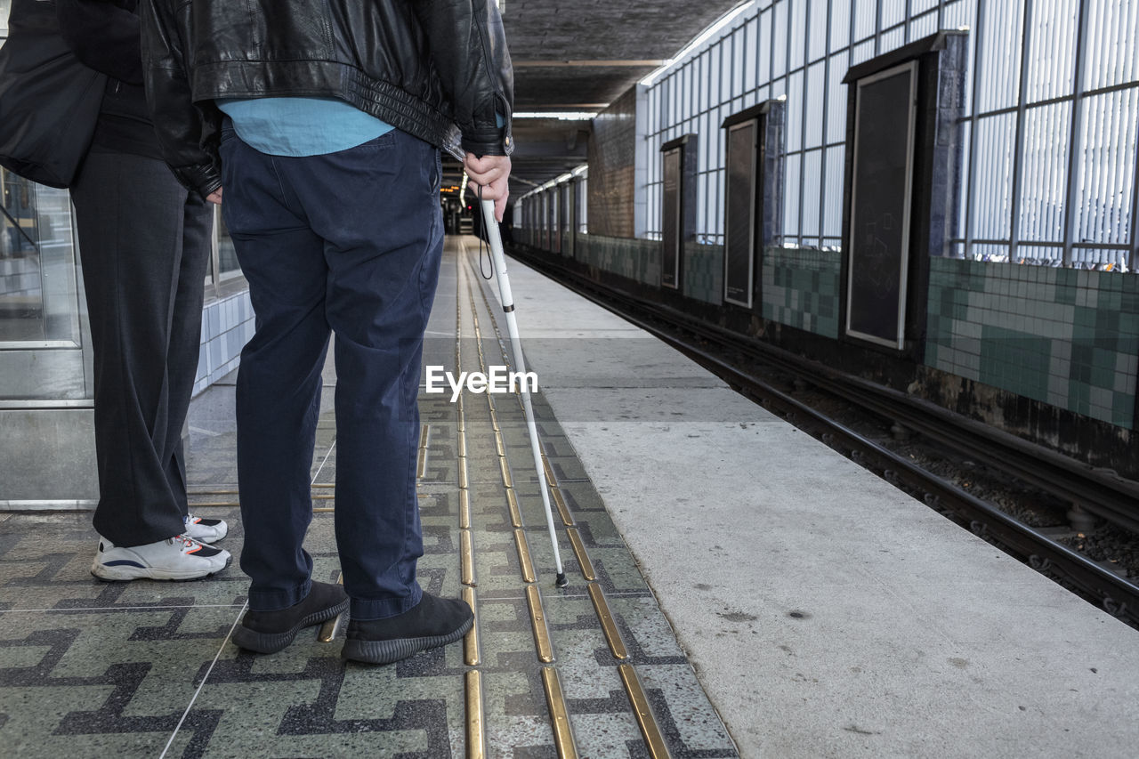 Man with white cane standing at train station