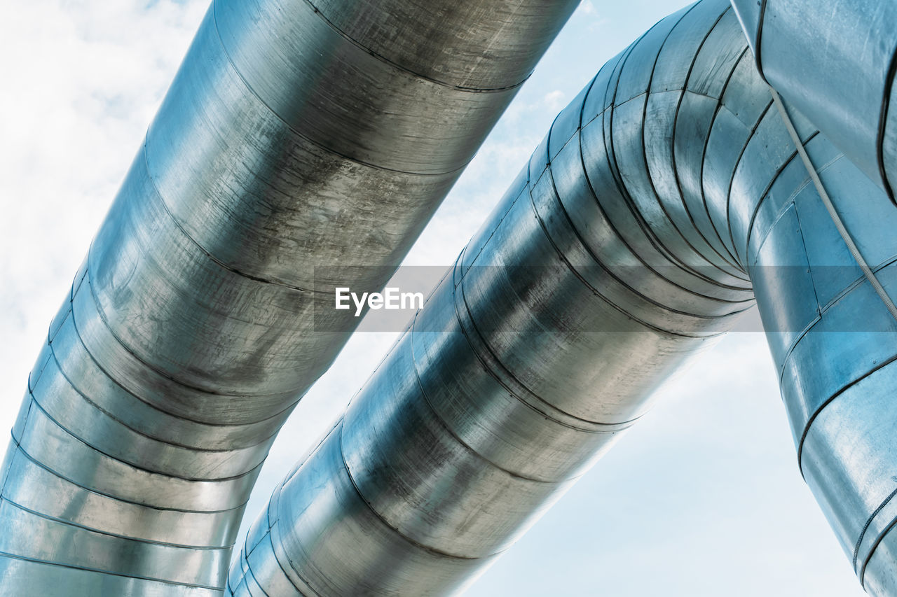 Low angle view of metallic pipes against sky