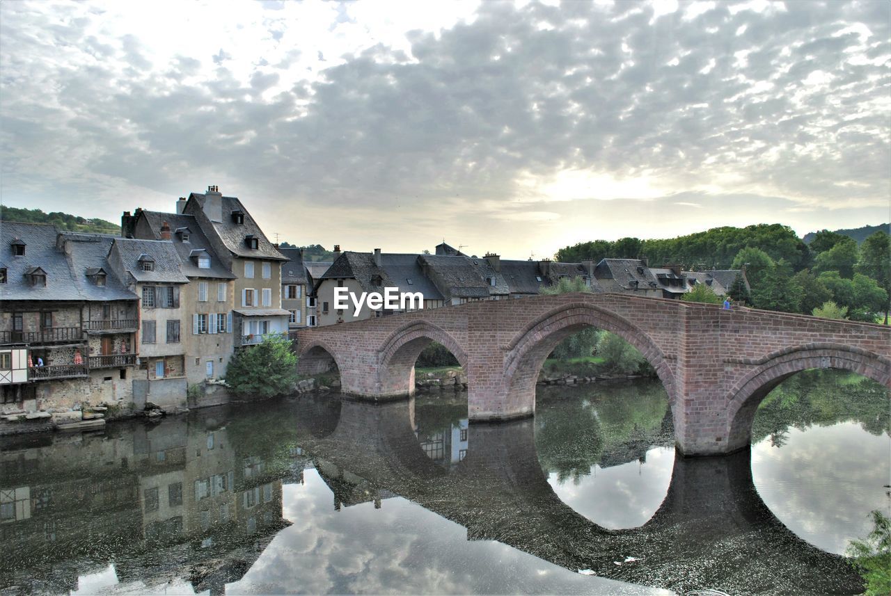 Arch bridge over river against cloudy sky