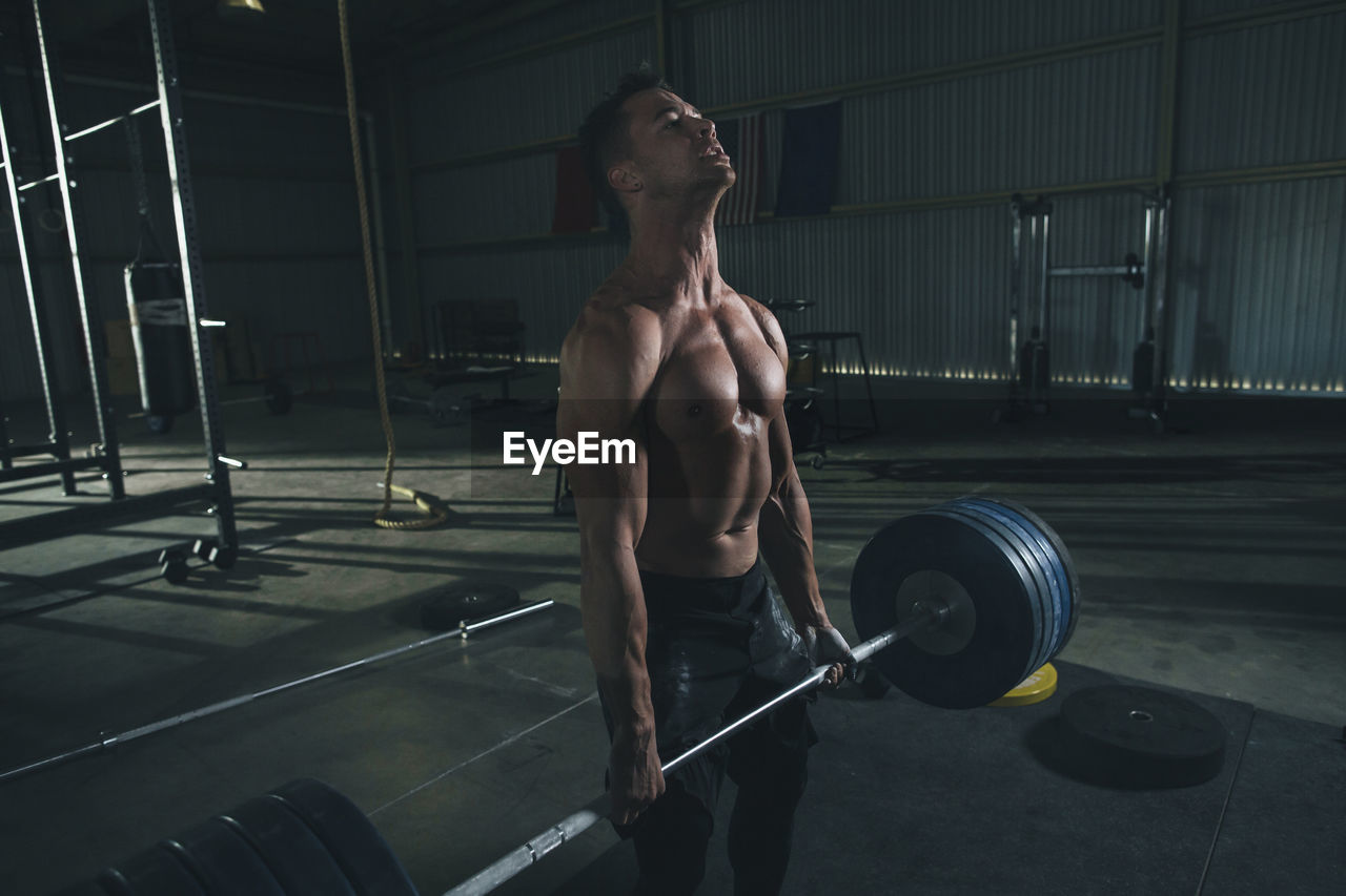 Shirtless male athlete lifting barbell in health club