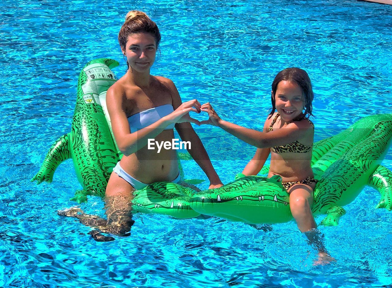 Portrait of siblings forming heart shape while sitting on inflatable raft