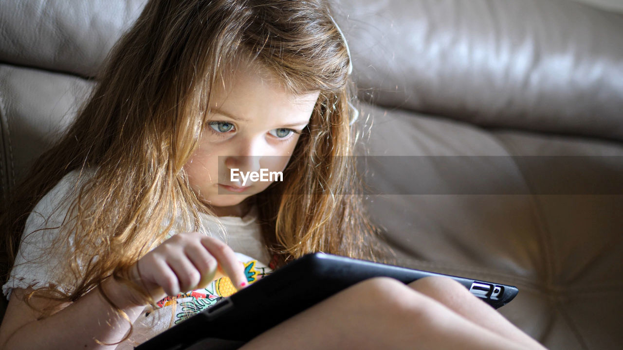 Little baby girl of three years playing with the tablet on the couch. growth issues and education.