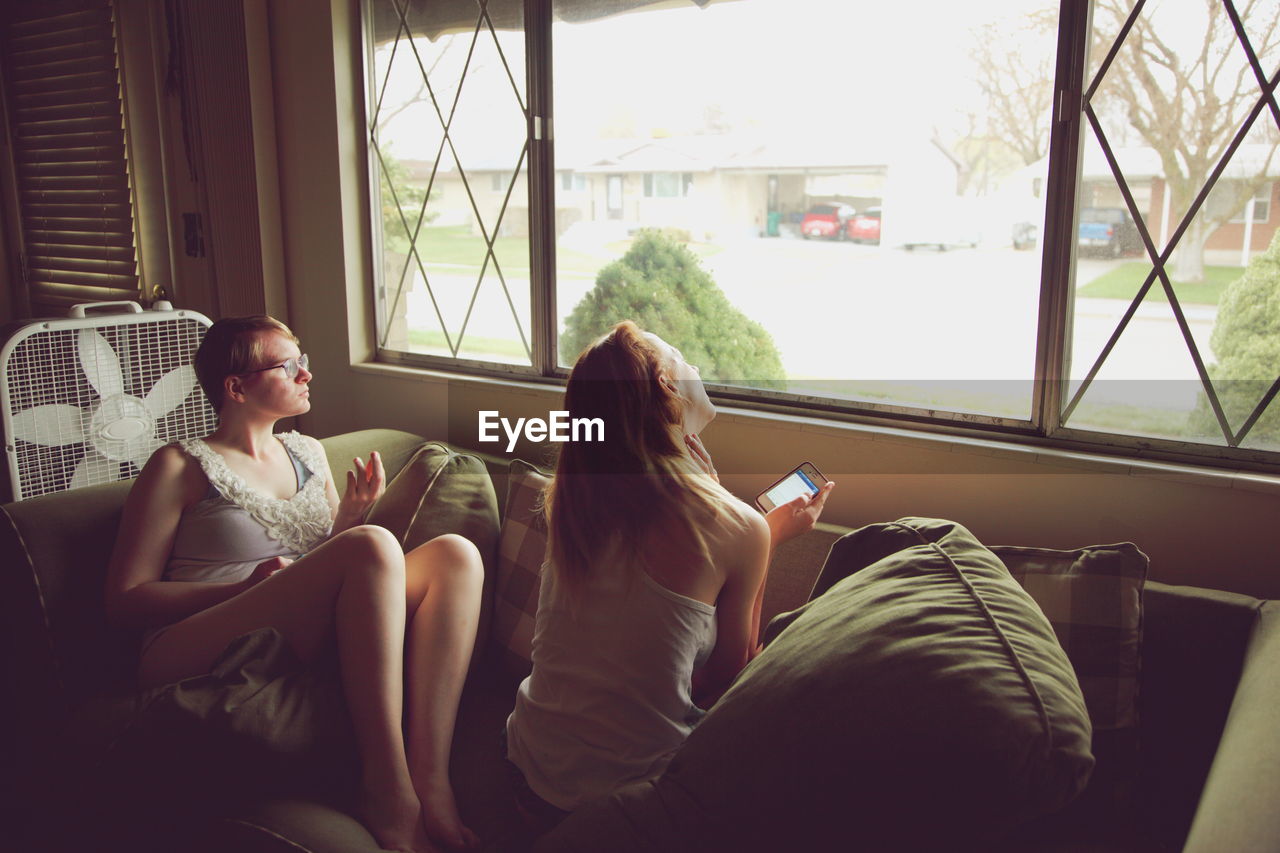 Sisters relaxing on sofa by window at home