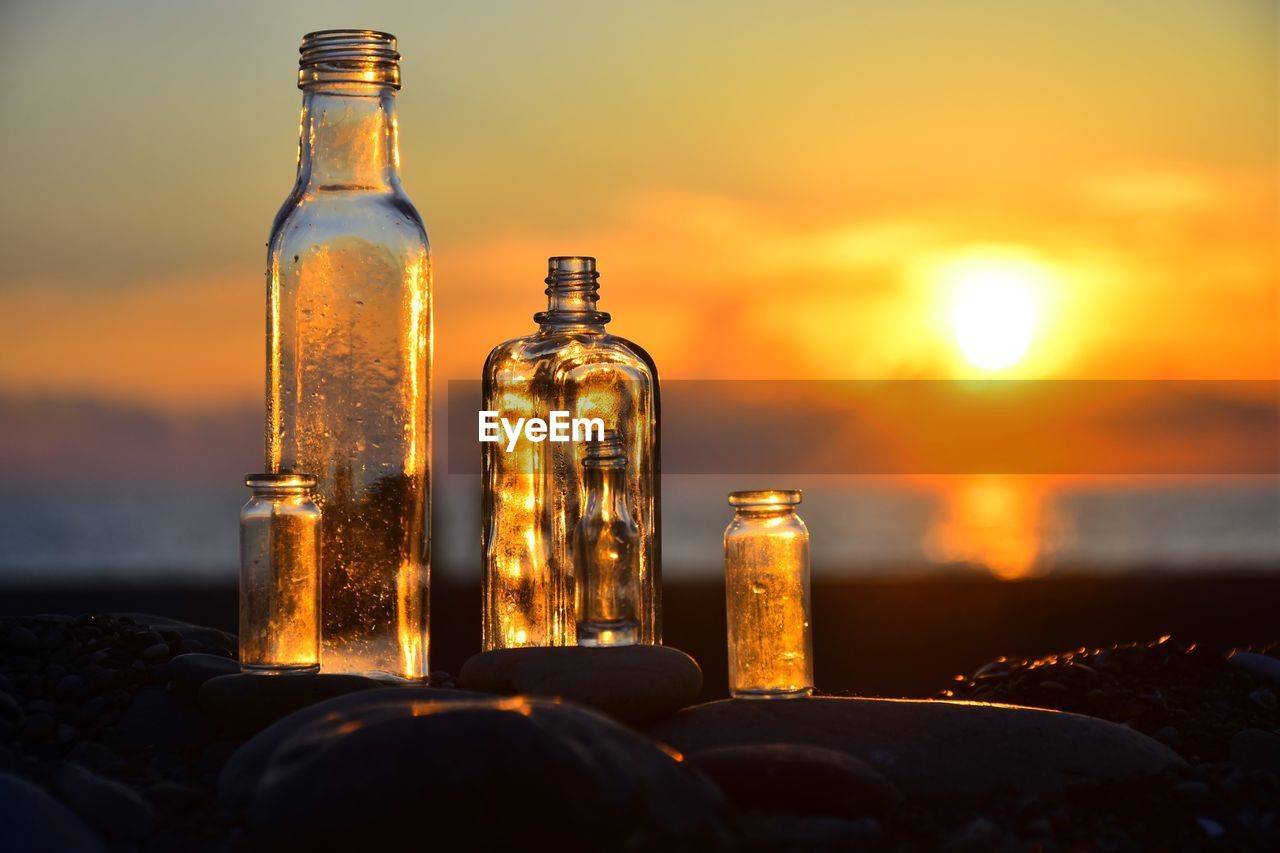 Close-up of empty bottles on table against orange sky