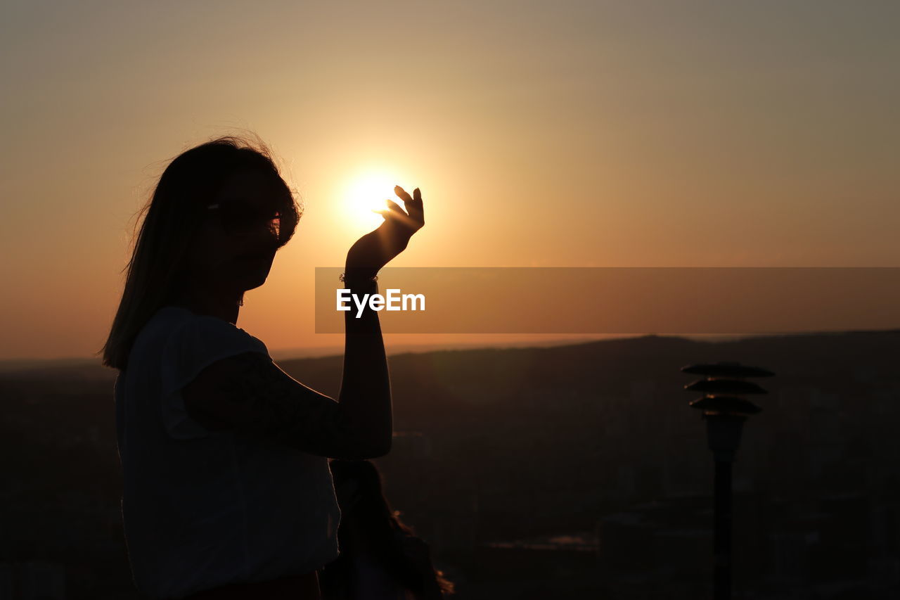 Side view of silhouette woman holding sun during sunset