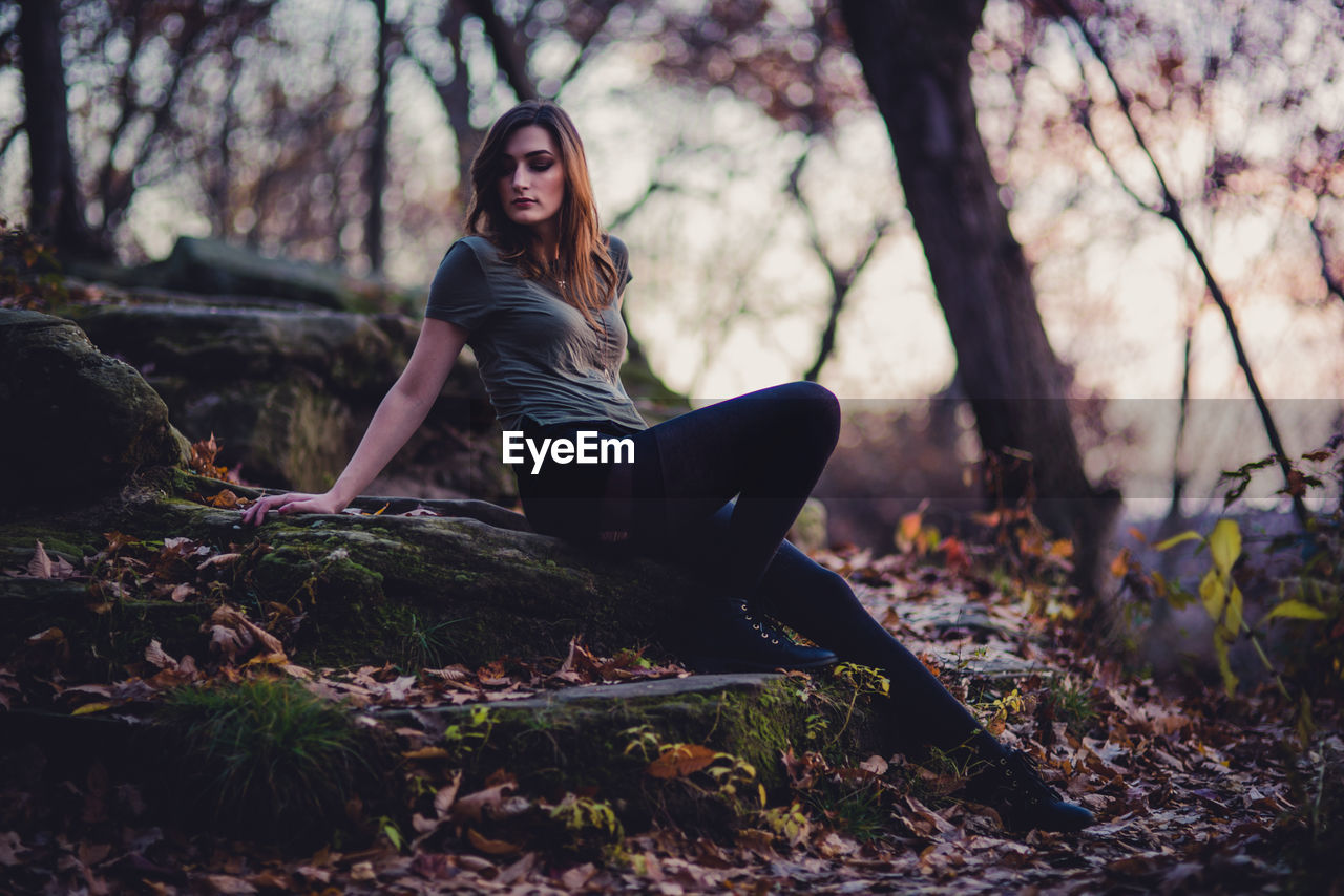 Full length of young woman sitting on rock in forest