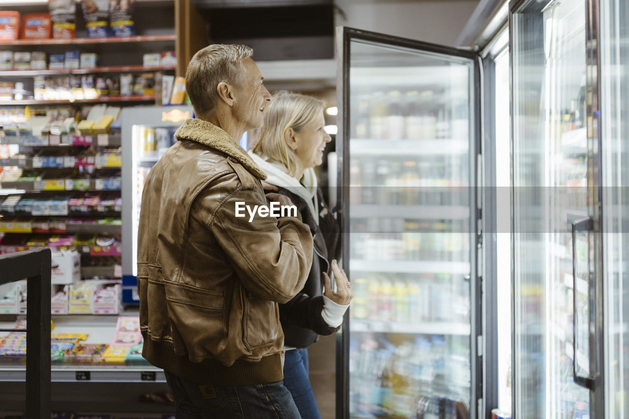 Smiling mature couple doing shopping from refrigerated section at supermarket