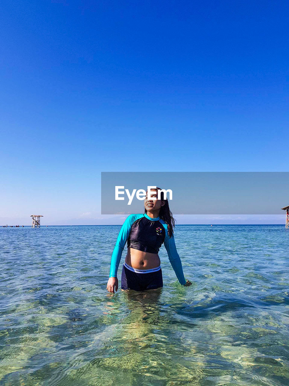 Smiling young woman in sea against clear blue sky