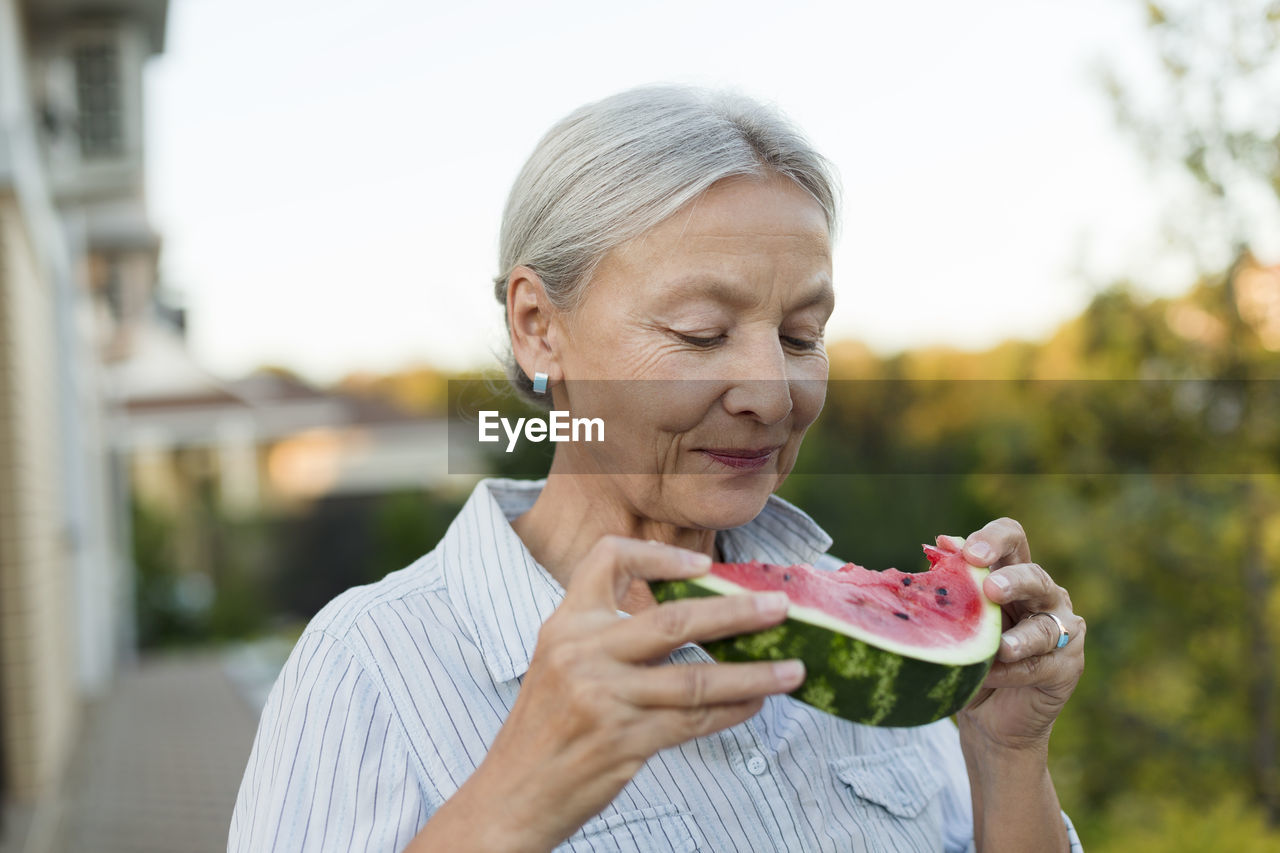 Portrait of senior woman eating watermelon slice in the garden