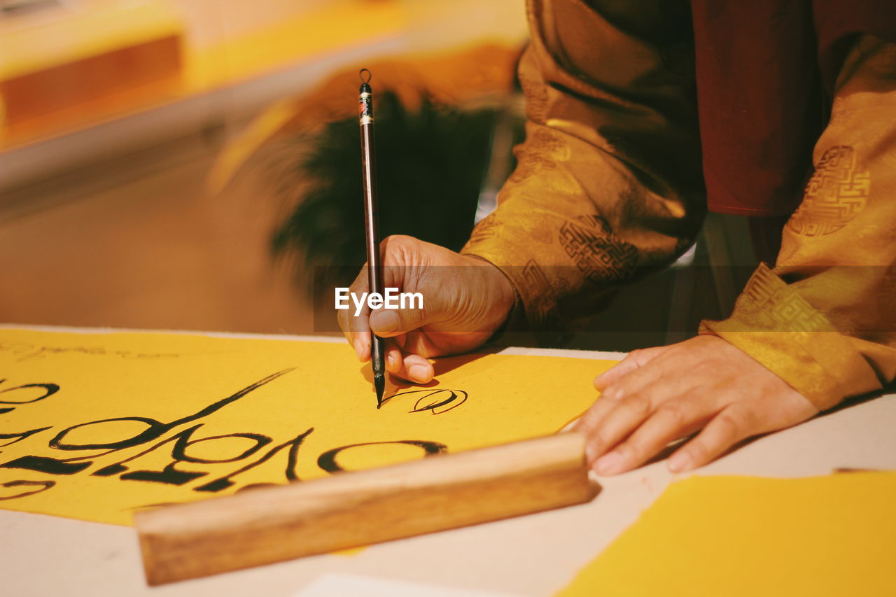 Midsection of man writing on yellow paper