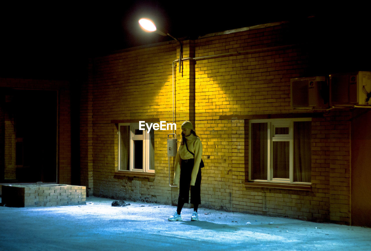 Full length of woman standing by building in city at night