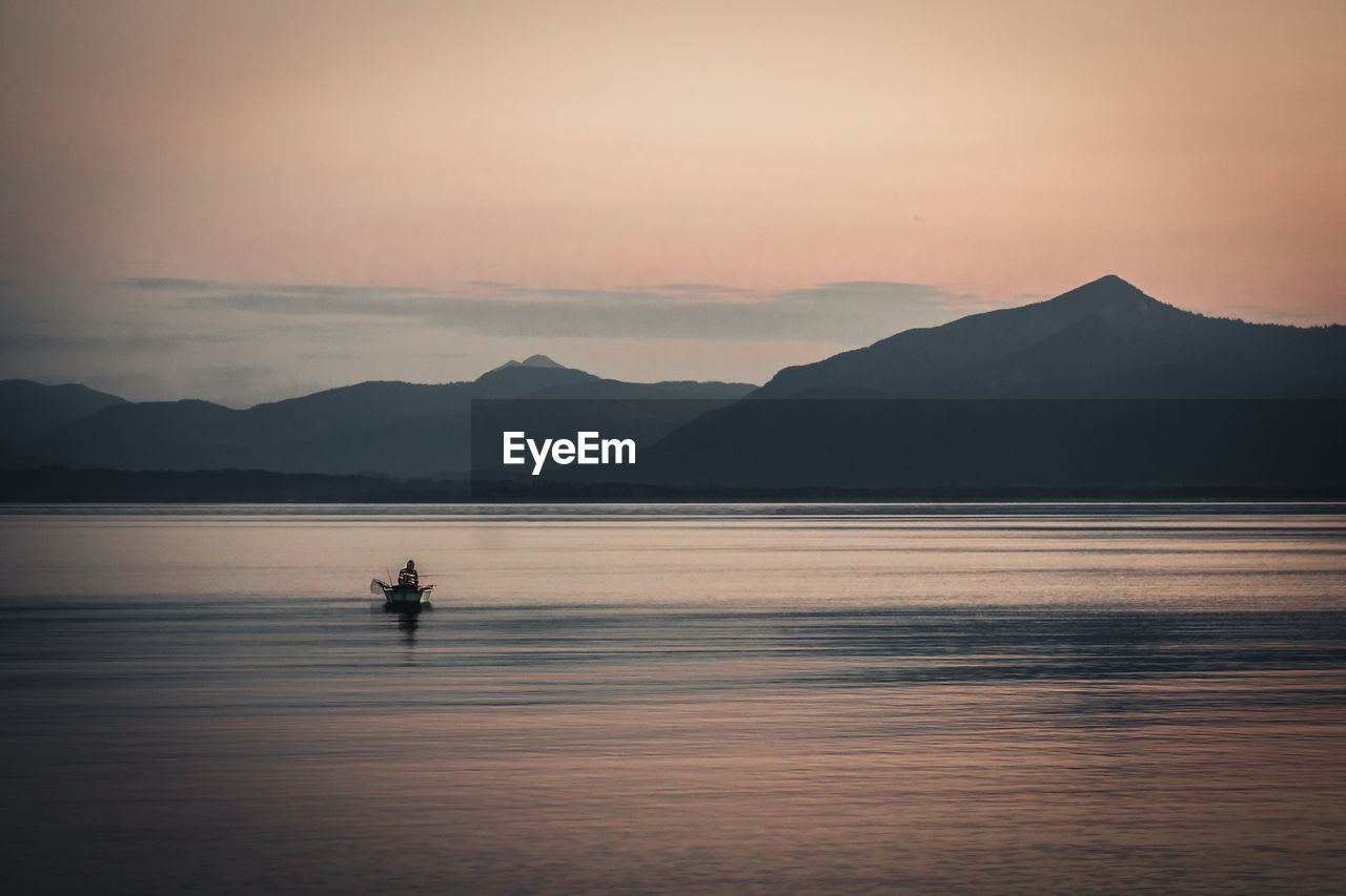 Silhouette person on boat in lake against sky during sunset