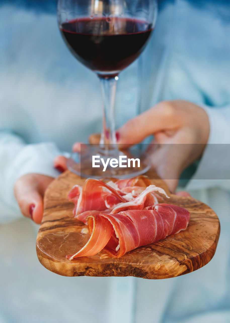 Close-up of wine glass and prosciutto on wooden serving board