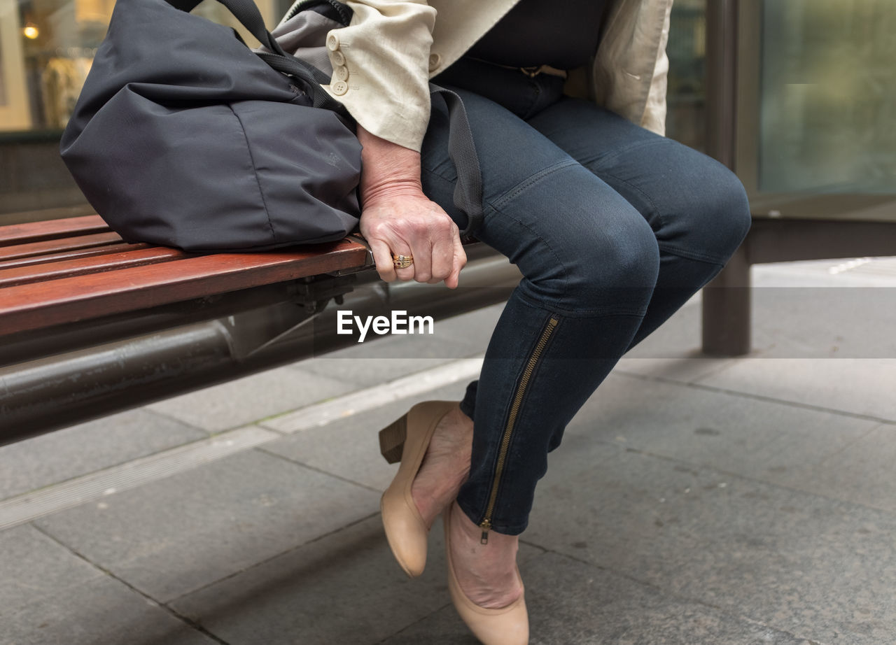Low section of woman sitting on bench in city