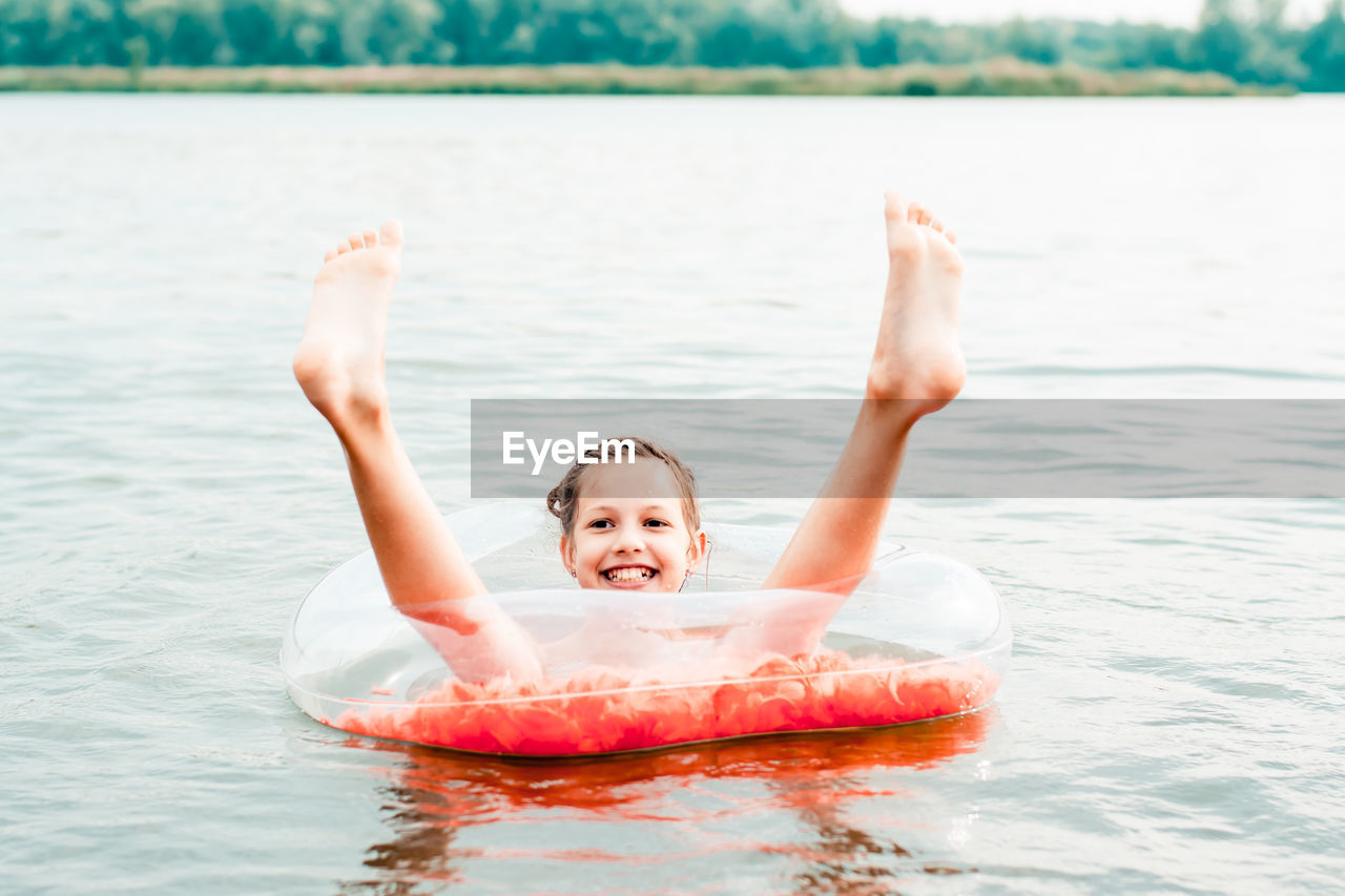 Cheerful girl sits in an inflatable ring with sticking legs in the river. local tourism. 