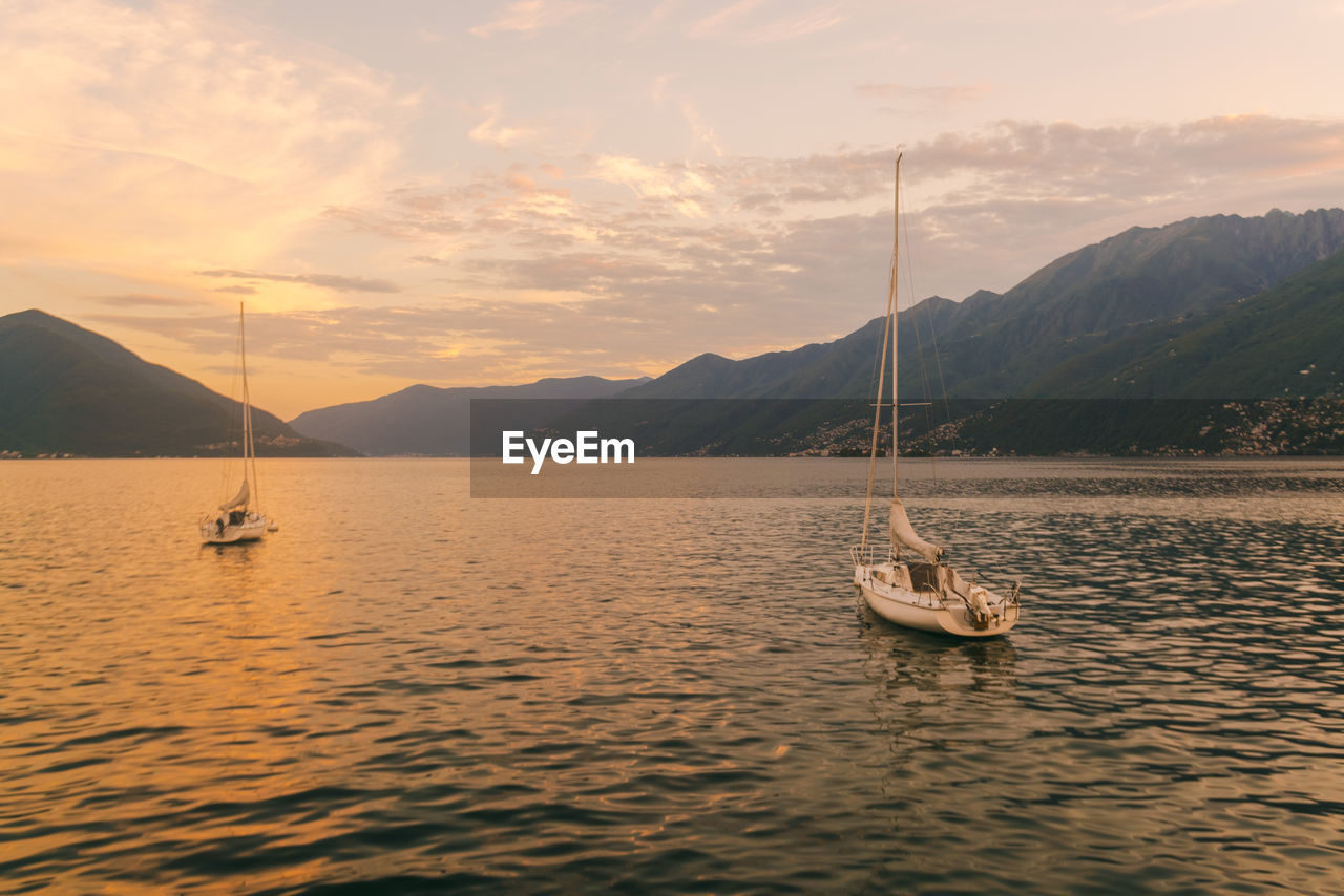 View of lake locarno at sunset with sailing boats and mountains