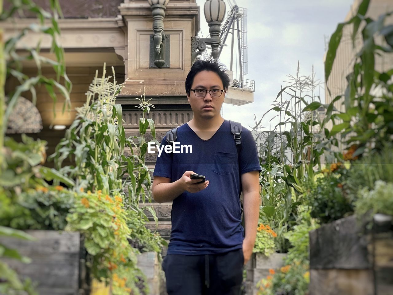 Portrait of young asian man standing between flowering plants against buildings in the city.
