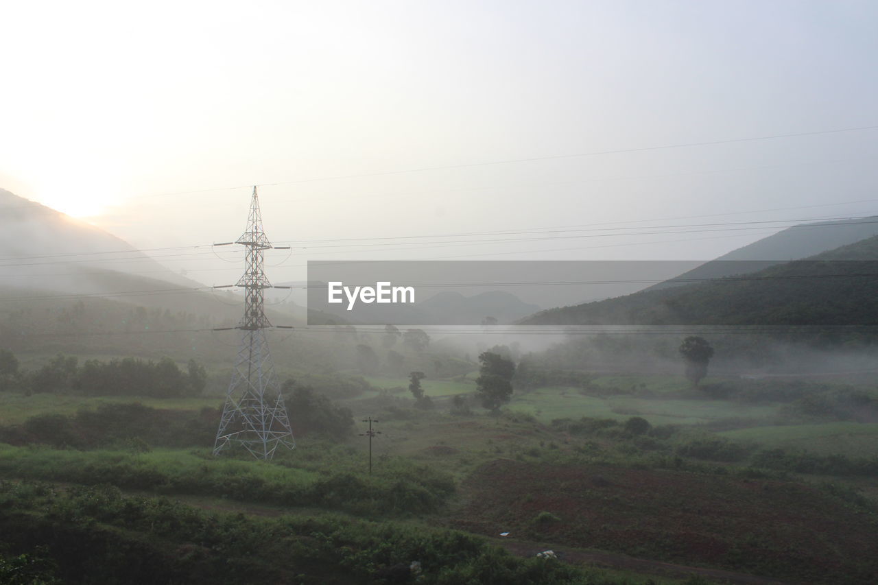 ELECTRICITY PYLONS ON FIELD AGAINST SKY DURING FOGGY WEATHER