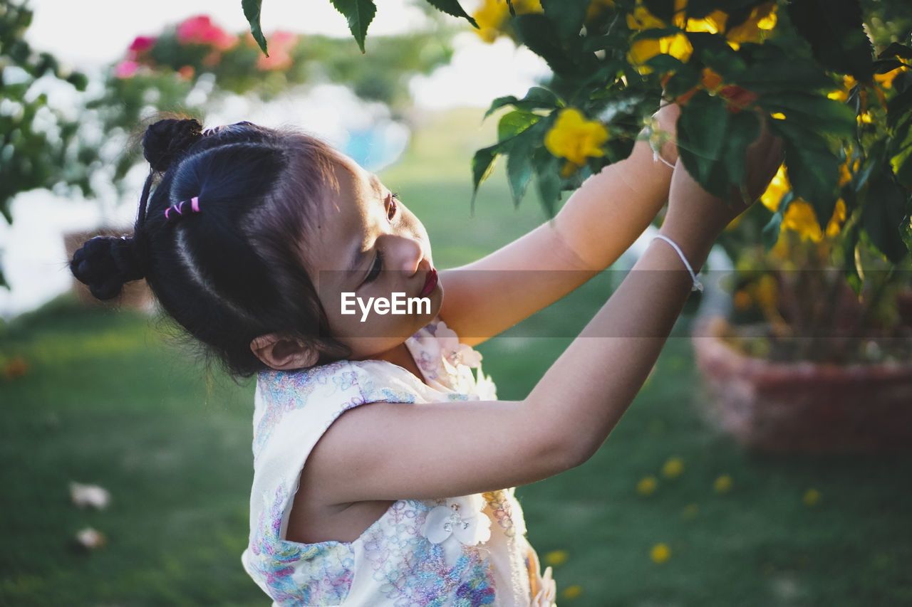 Side view of girl plucking flowers from plant at park