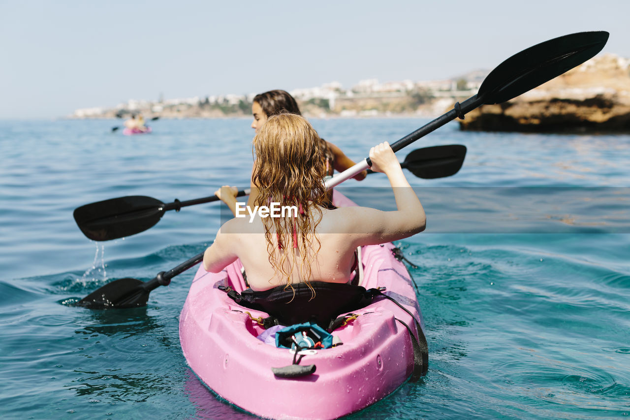 Back view travelers with paddles floating on turquoise seawater near the rocky shore on sunny day in malaga spain