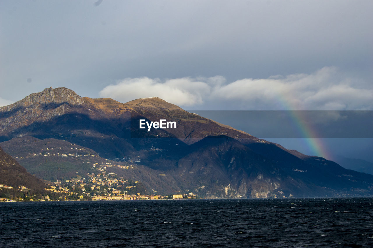 Scenic view of rainbow over sea and mountains against sky