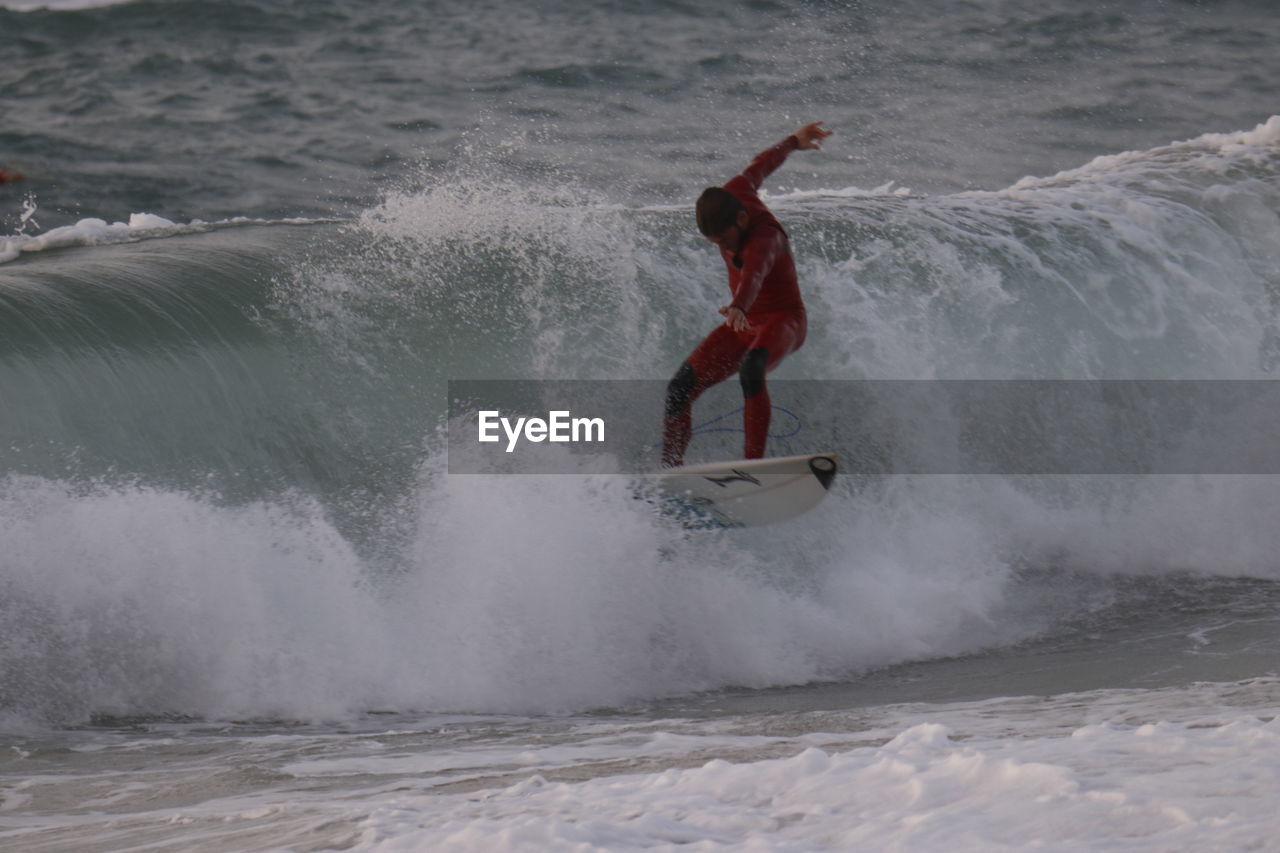 FULL LENGTH OF MAN SURFING ON SEA WAVES