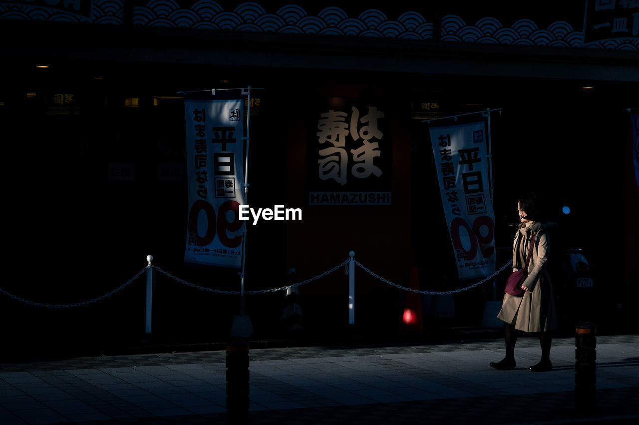 PEOPLE STANDING ON ILLUMINATED STREET IN CITY