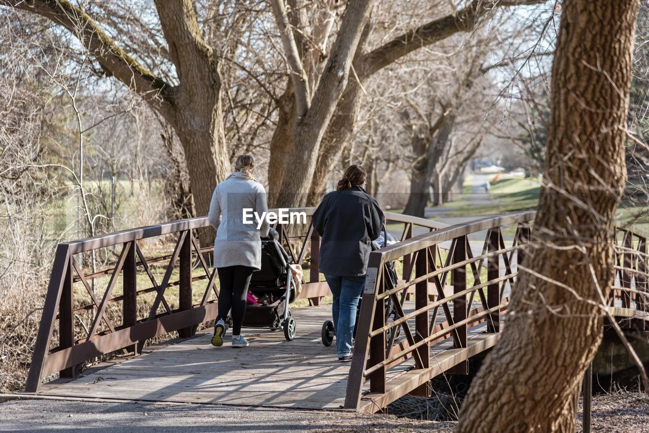 Rear view of woman walking with prams on footbridge