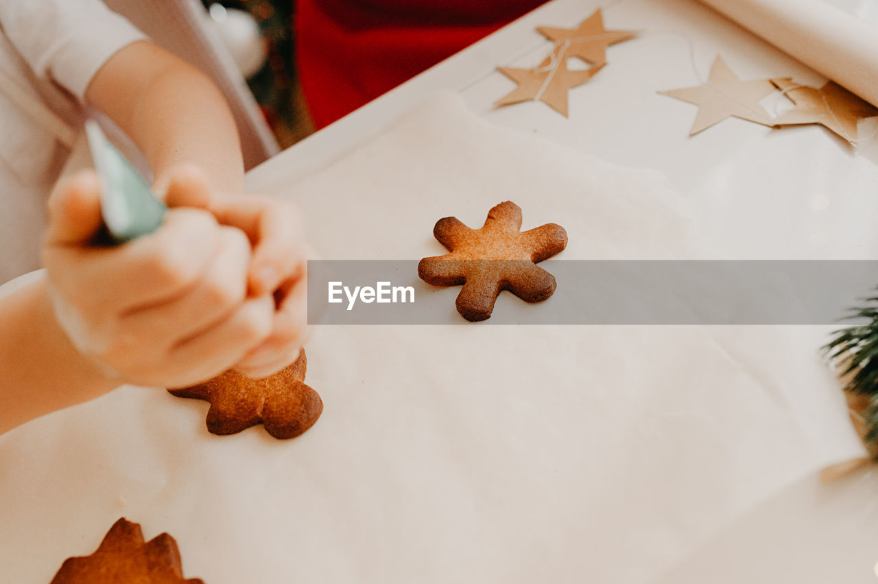 A child squeezes food dye from a tube onto a finished gingerbread cookie on a white table