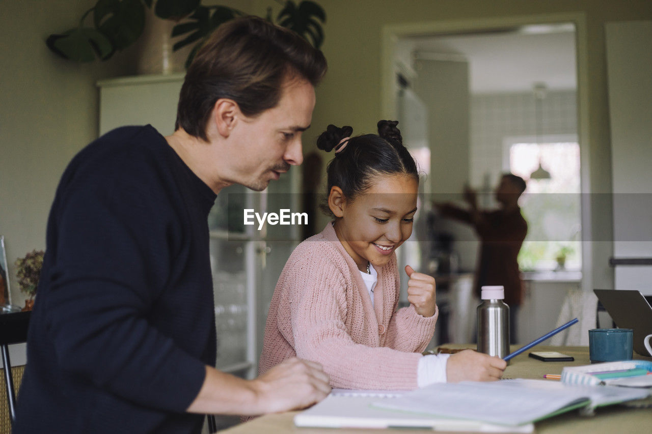 Father sitting next to excited daughter doing homework at home
