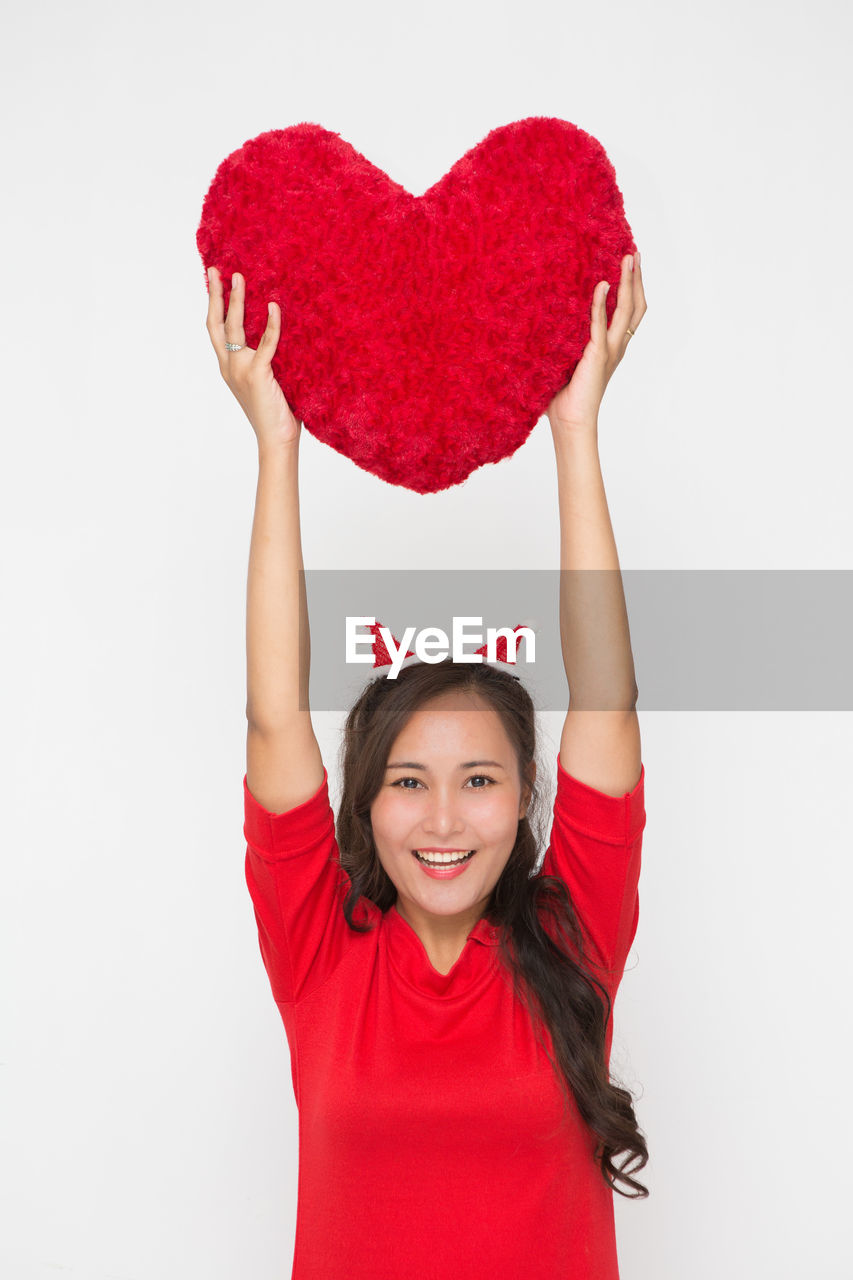 emotion, positive emotion, heart shape, red, happiness, smiling, portrait, one person, valentine's day, women, studio shot, indoors, white background, celebration, cheerful, pink, love, clothing, looking at camera, child, heart, waist up, female, adult, joy, front view, arms raised, arm, young adult, copy space, cut out, human limb, person, fun, limb, holding, childhood, holiday, excitement, event, enjoyment, creativity