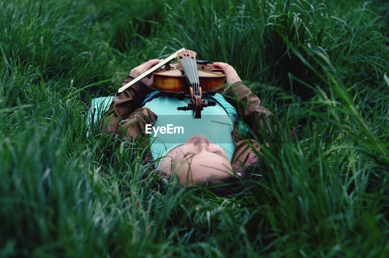 Woman holding violin lying on grassy field