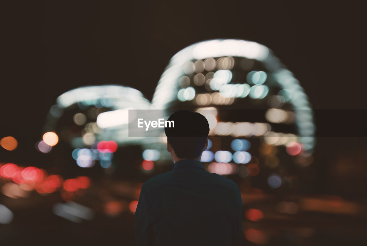 Rear view of man standing against illuminated buildings in city