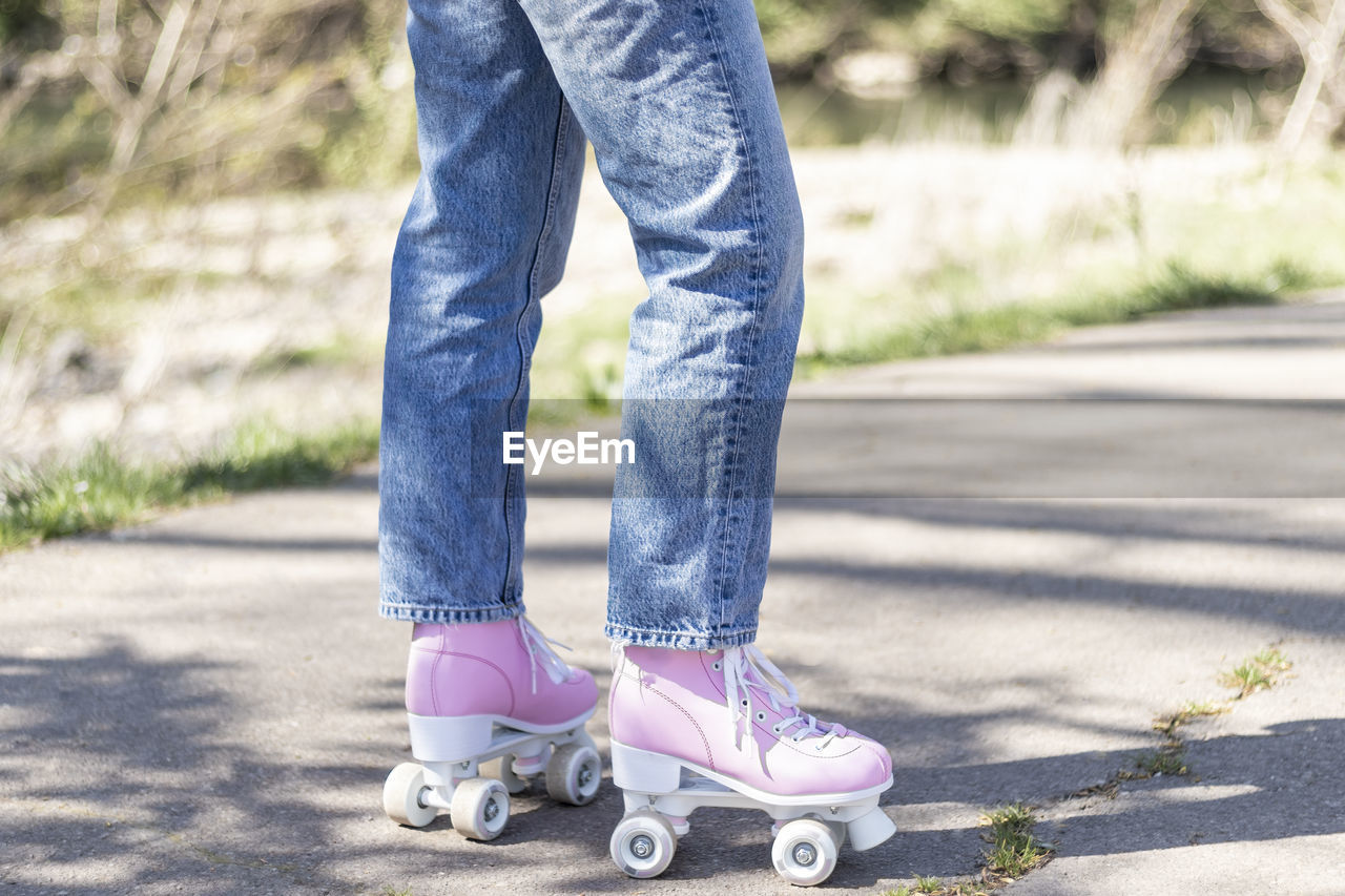 Woman's legs in jeans and pink roller skates in a park