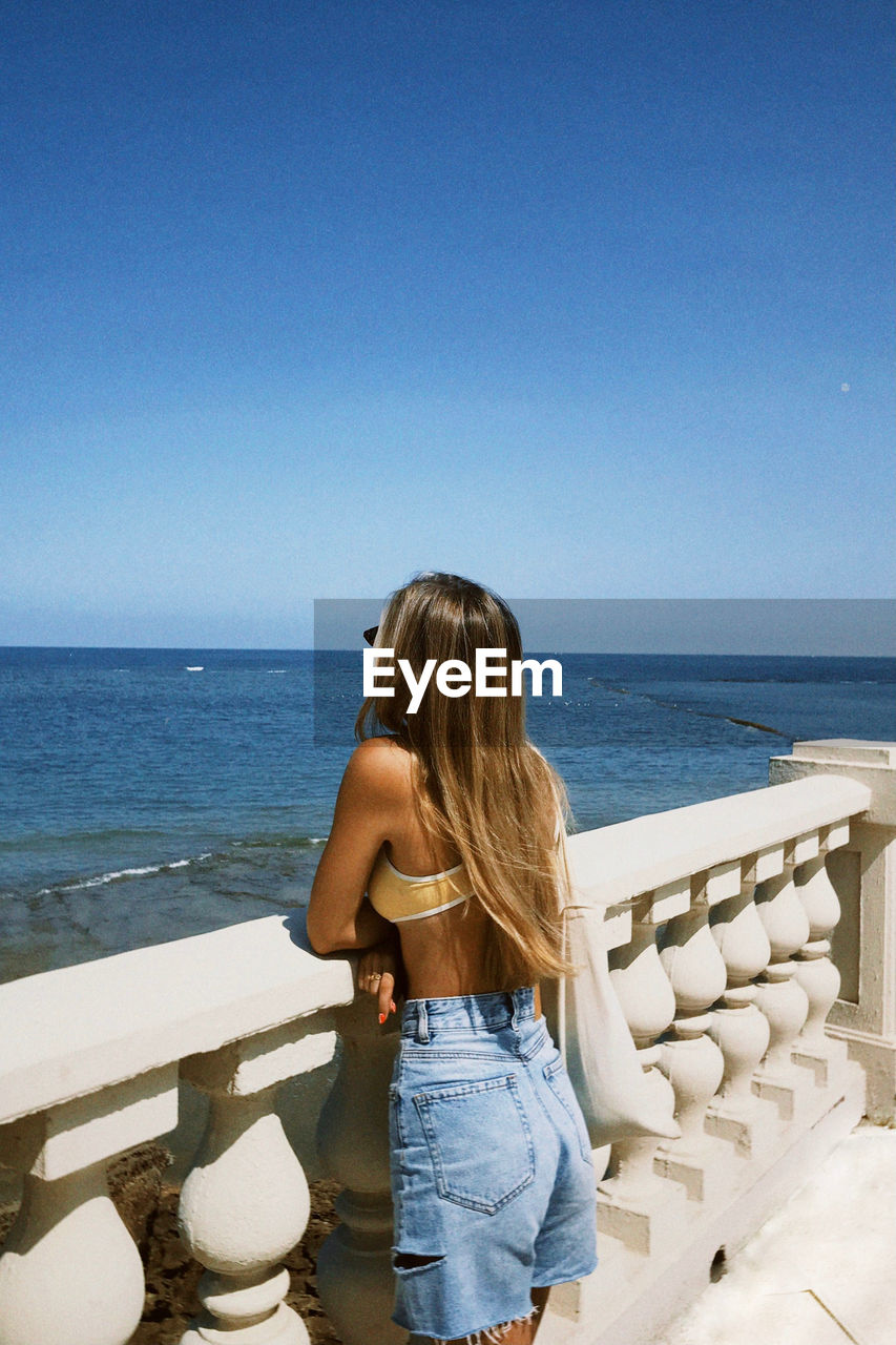 Vintage photo of a blonde girl looking at the sea wearing bikini top and shorts surfer style blogger 