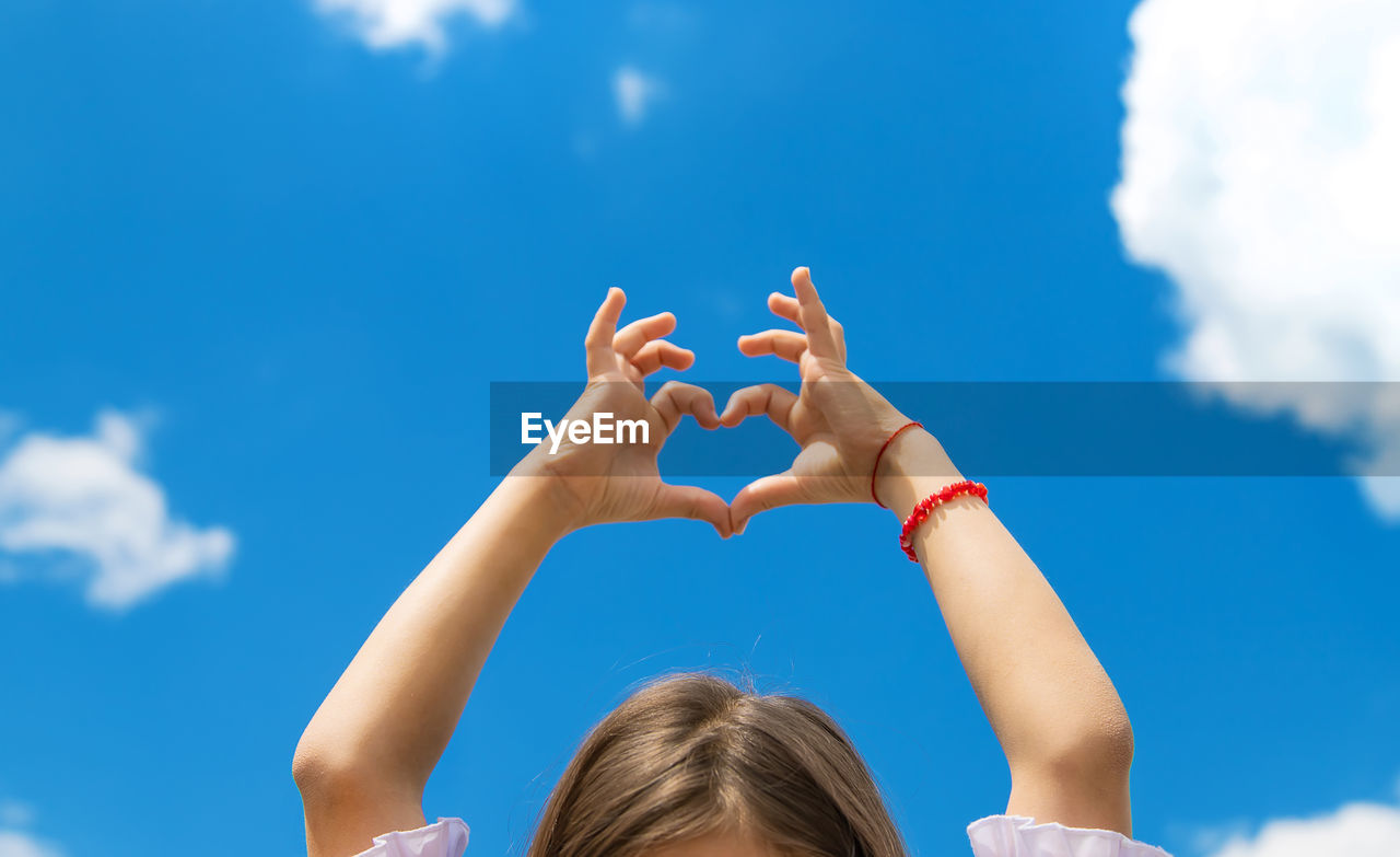Low angle view of girl making heart shape against sky