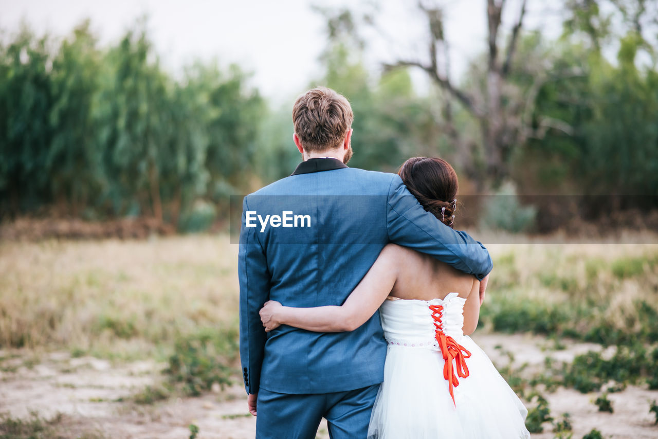 Rear view of newlywed couple on field against trees