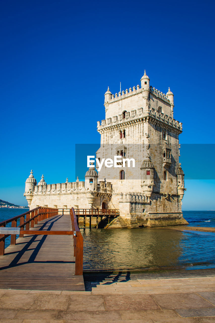 Buildings by sea against clear blue sky