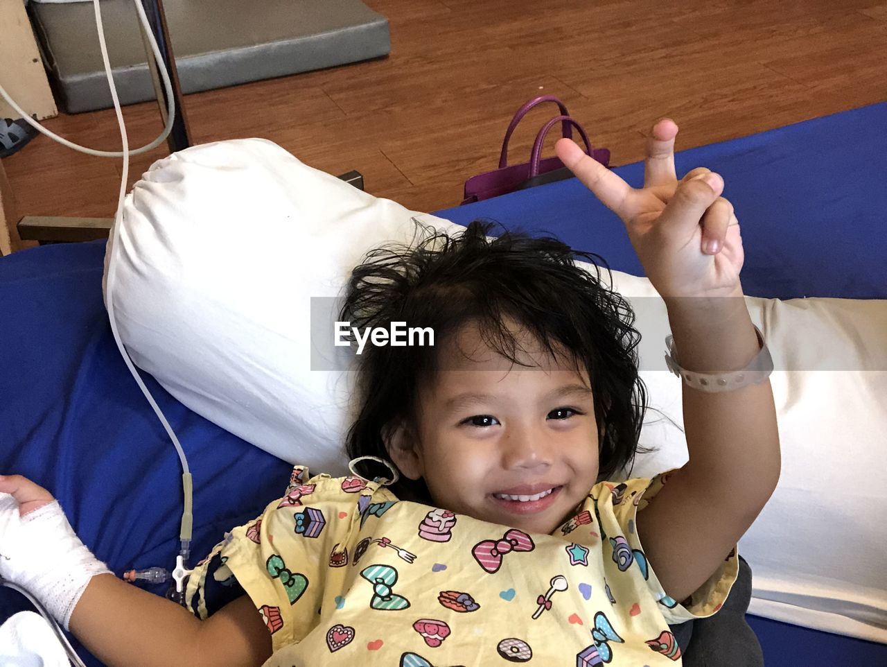 High angle portrait of girl showing peace sign while lying on bed in hospital